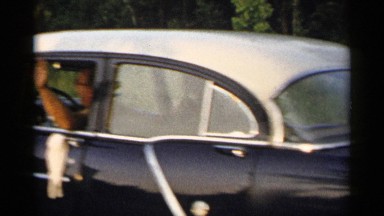 1954: a man waving as he is driving off with two boys sitting in the trunk
