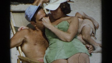 1954: a woman sits in a man's lap on the beach on a sunny day NEW YORK