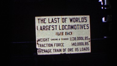 1960: a large antique locomotive is observed from a road by several men