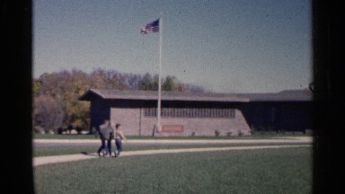 1960: some people walk the green grasses ground near to big building and sky