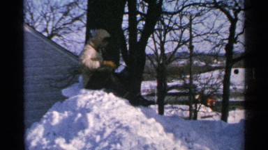 1965: boy sitting in top of snow load and making a snowball and throw it