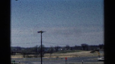 1964: a car moving through the road in a vast area with houses in the distant