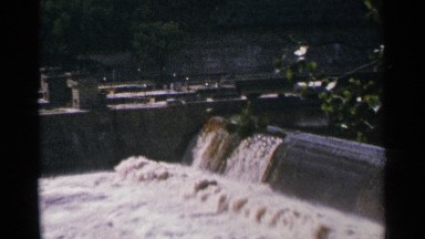 1964: murky water flows swiftly over a barrier in a dam on a river MINNESOTA