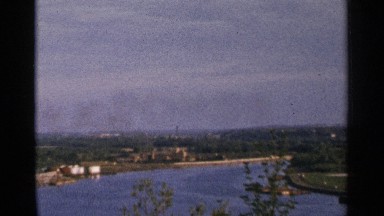 1964: waterside industrial city area with side forest with trees on a shiny day