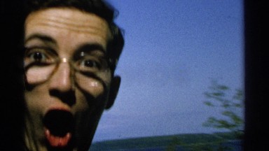 1964: specked young man showing a beautiful nature mountain and trees in camera