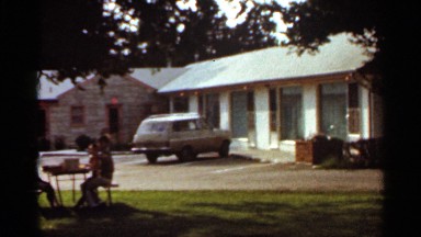 1965: people sitting at a table in the shade outside of a building