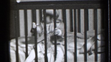 1939: a baby girl sits holding the balusters of the crib, the baby looks around