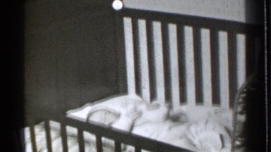 1939: sleepy baby waking up inside a crib playing with his or her toy. DANIELSON