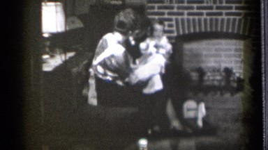 1939: woman flaps apron hem to entertain baby held by man while other watch
