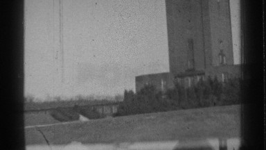 1939: squat tower stands in the middle of an open field with some shrubs