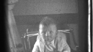 1939: baby sitting on a high chair , playing with an object in his hand.