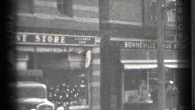 1939: people do their shopping at classic little stores and glance at cars