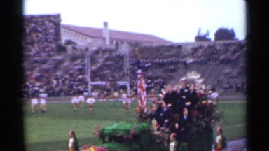 1944: float with people on it passing a football game on a football field.