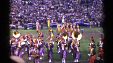 1944: marching band wearing blue satin outfits and red fezzes cross stadium