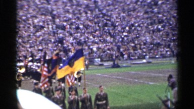 1944: marching band in american football stadium led by color guard