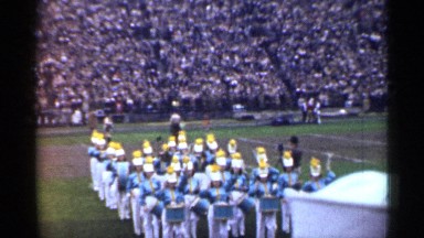 1944: marching band playing music by a football field in front of crowds