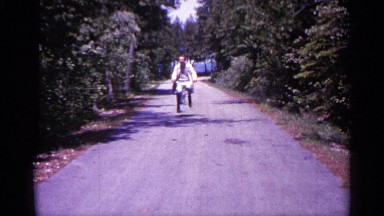 1960: a man joyously riding bike on a lonely road surrounded by plants. MICHIGAN