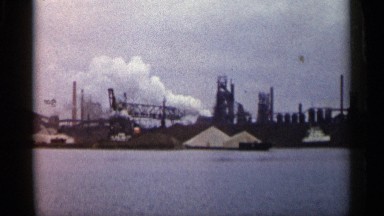 1960: industrial area near water with cranes and white sand stack