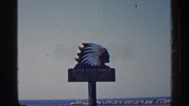 1960: old film capture of native american themed location sign over black river