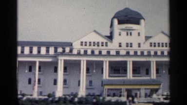 1960: grand white building has row of columns between waving american flags