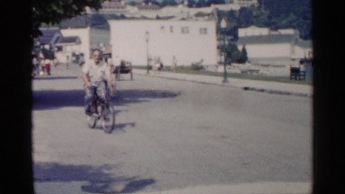 1960: the man drive in the cycle slow the road on side house shop another place