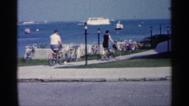 1960: two friends walking their bikes down a road by a gazebo on the beach.