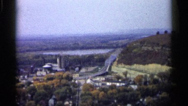 1961: road leads to bridge leaving small town and continues around mountain