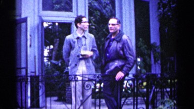 1961: a man hiding something on his back and talking to another man