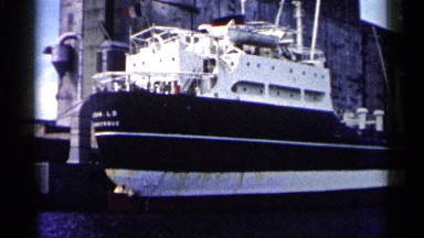 1961: a tall, black and white boat is seen docked next to a tall stone structure