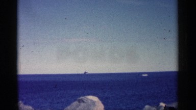 1961: blue sky shiny day seaside with small rocks boats are passing by the area