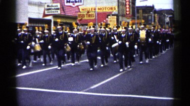1961: band members march down the street during a parade playing music loudly.