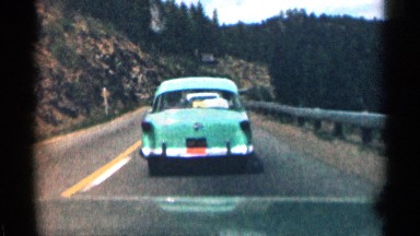 1963: cars driving down a road as a motorcycle passes going in opposite