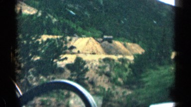1963: a car slow run near to hills in green grasses huge for mountain road side
