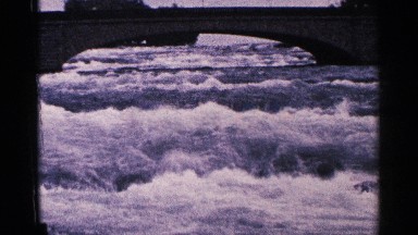 1964: water rushing down a stream under a overpass bridge
