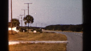 1966: a road at the center and trees are both side a car moving fast on the road