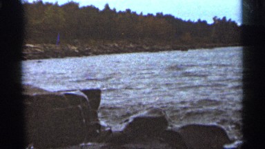 1965: body of water moving next to a forest forming small waves