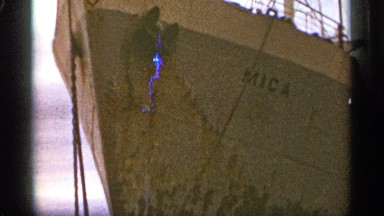 1965: a ship resting in harbor and some yellow dressed persons goes near it