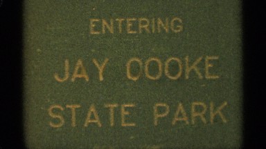 1965: a video introduction scene which includes a banner sign of jay cook state