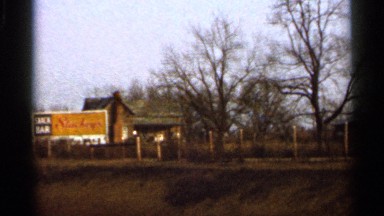 1966: a bar shop with bright sign board in front and tall trees surrounds it