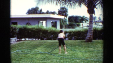 1963: children are playing with hosepipe at a residential area beside grass lawn
