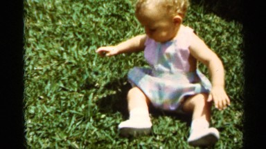 1963: a small child sitting on the grass and looking the surface around it