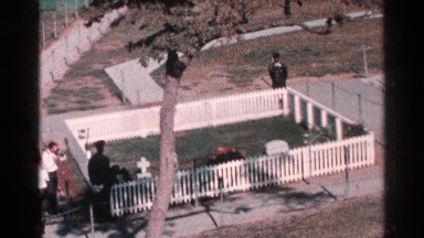 1964: many people are looking in a strip mess protected ground with tomb stone