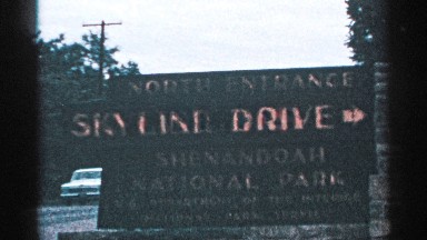 1964: a sign board represents skyline drive and a car moving backside