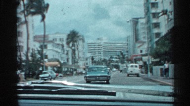1958: the view from the front seat of a vehicle traveling down a city street