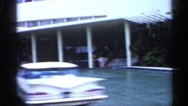 1958: a car drives quickly past buildings and other cars FLORIDA