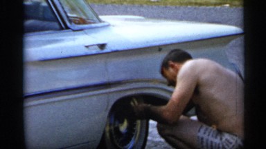 1958: a man cleaning his car containing glass window wheel sitting on its side