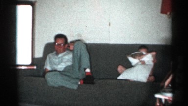 1958: man sitting on a couch with a baby that is playing with pillow. NEW JERSEY