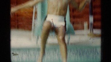 1963: a young boy comes down a slide and enters a pool and then starts swimming