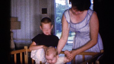 1959: brother is standing beside a baby cot and mother is taking care of