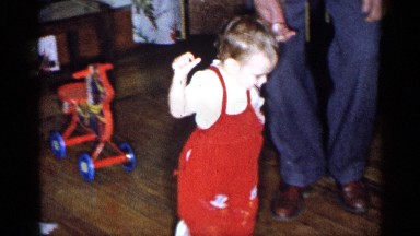 1955: toddler learning to walk with the help of father at home